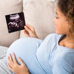 African-american pregnant woman holding ultrasound scan at home
