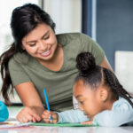 Tips for choosing a summer sitter Hispanic young adult woman babysitting child and helping with homework