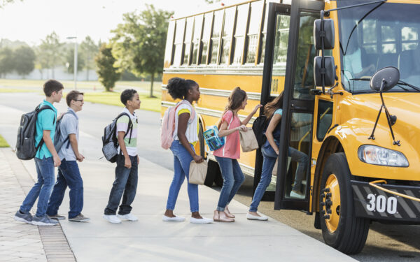 A diverse group of six middle school students, 11 to 13 years old, boarding a yellow school bus.