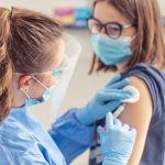 Female halthcare employee applies vaccine from injection into the arm of a young girl.