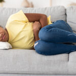 Black Girl Suffering From Abdominal Pain Lying On Sofa Indoor