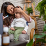 Virtual visits are perfect for today’s busy families Worried mother talking to doctor on laptop and taking baby's temperature during telemedicine session