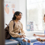 Young adult female patient smiles while listening to the nurse give an encouraging update regarding her medical exam
