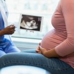 Focus on foreground as doctor shows ultrasound in background