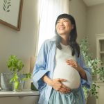 Pregnant woman cradles baby bump while smiling.