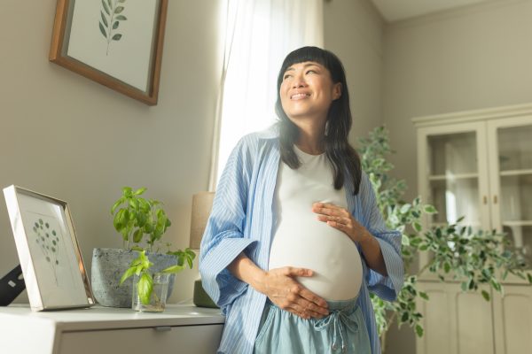 Pregnant woman cradles baby bump while smiling.