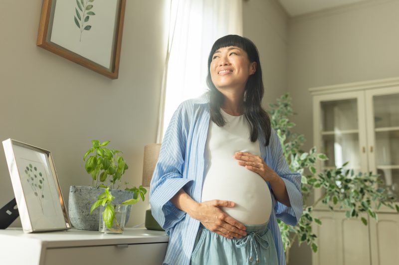 Pregnant woman cradles baby bump while smiling.