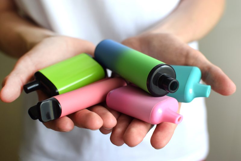 Many colorful electronic cigarettes in the hands of a teenager. Vaping with nicotine. Danger for teenagers.