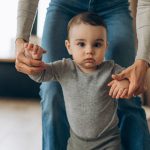 GettyImages - mom helping toddler son walk