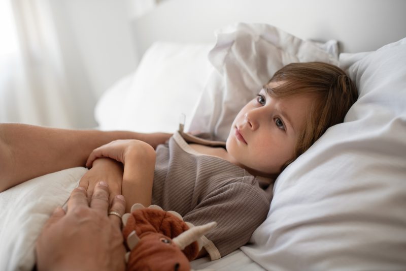 Sad little boy  in bed with stomachache, flu, cold, coronavirus, bronchitis or pneumonia, virus or infectious disease, measuring temperature