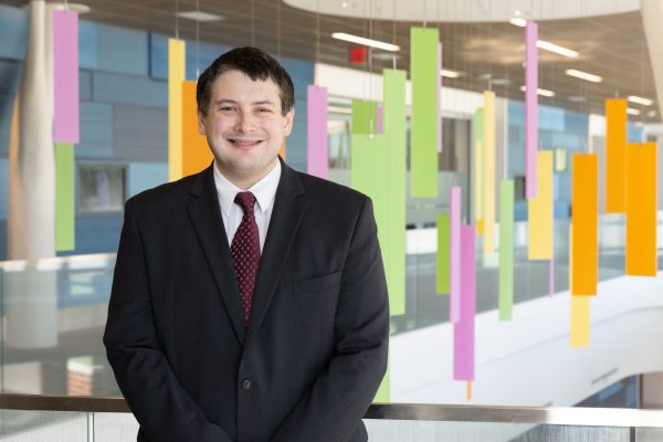 Dr. Christopher Costin smiling at the camera is a black suit and red tie in the Kay Jeweler’s Pavilion on the Akron Children’s Golisano Campus.