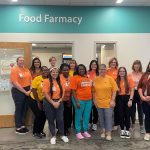 Hunger Action Awareness Month The Food Farmacy standing together and smiling in front of a door labeled "Food Farmacy" at Akron Children's. They are wearing orange shirts and name badges.