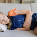 Stomachaches and children: What parents should know Teen girl lying on sofa at home holding stomach with eyes closed