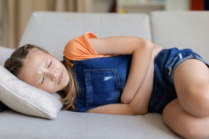 Teen girl lying on sofa at home holding stomach with eyes closed