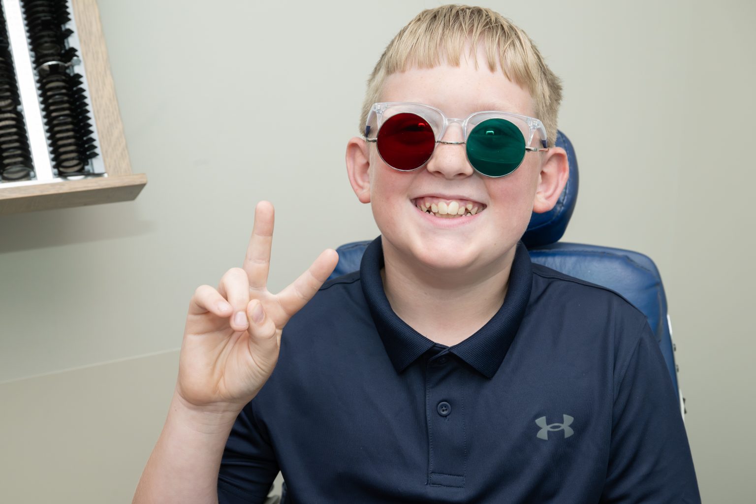 Akron Children's Vision Center patient Jake Morrison, giving the peace sign at a checkup wearing glasses with one red lens and one green lens.