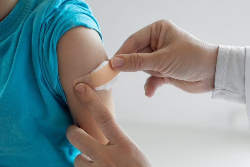 A doctor's hand is shown putting a band aid with a cotton ball on shoulder after successful vaccination.