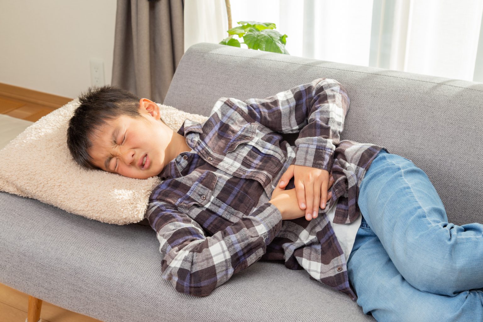 Middle-school aged boy lying on a sofa, holding his stomach and grimacing because he doesn't feel well.